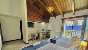 Un dormitorio con dos camas, un escritorio y una kitchenette.