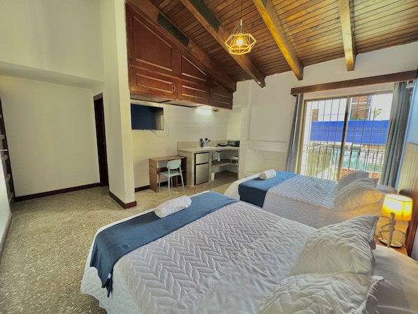 A bedroom with two beds, a desk, and a kitchenette. - Hotel Citadin Z10 (Guatemala City)