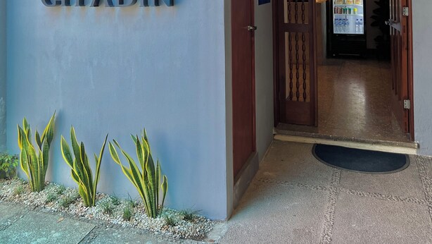 Una entrada de edificio moderno con un letrero 'CITADIN', un refrigerador lleno de bebidas y una pequeña zona ajardinada con plantas.