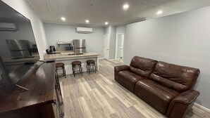A modern kitchen with a central island, bar stools, and a brown leather sofa.
