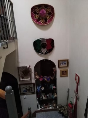 Una escalera con barandilla metálica, una pared con dos placas decorativas, un estante con varios objetos y un extintor.