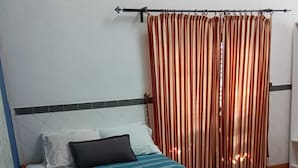 Una cama con un edredón azul y verde claro a rayas, dos toallas rojas y una cortina a rayas.