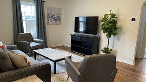 Un salon moderne avec un téléviseur à écran plat, des canapés gris, une table basse et une grande plante verte.