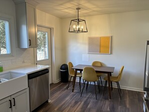 A modern kitchen with a dishwasher, a dining table with four chairs, and a pendant light. - Cozy home in historic Hillsdale (Hillsdale)