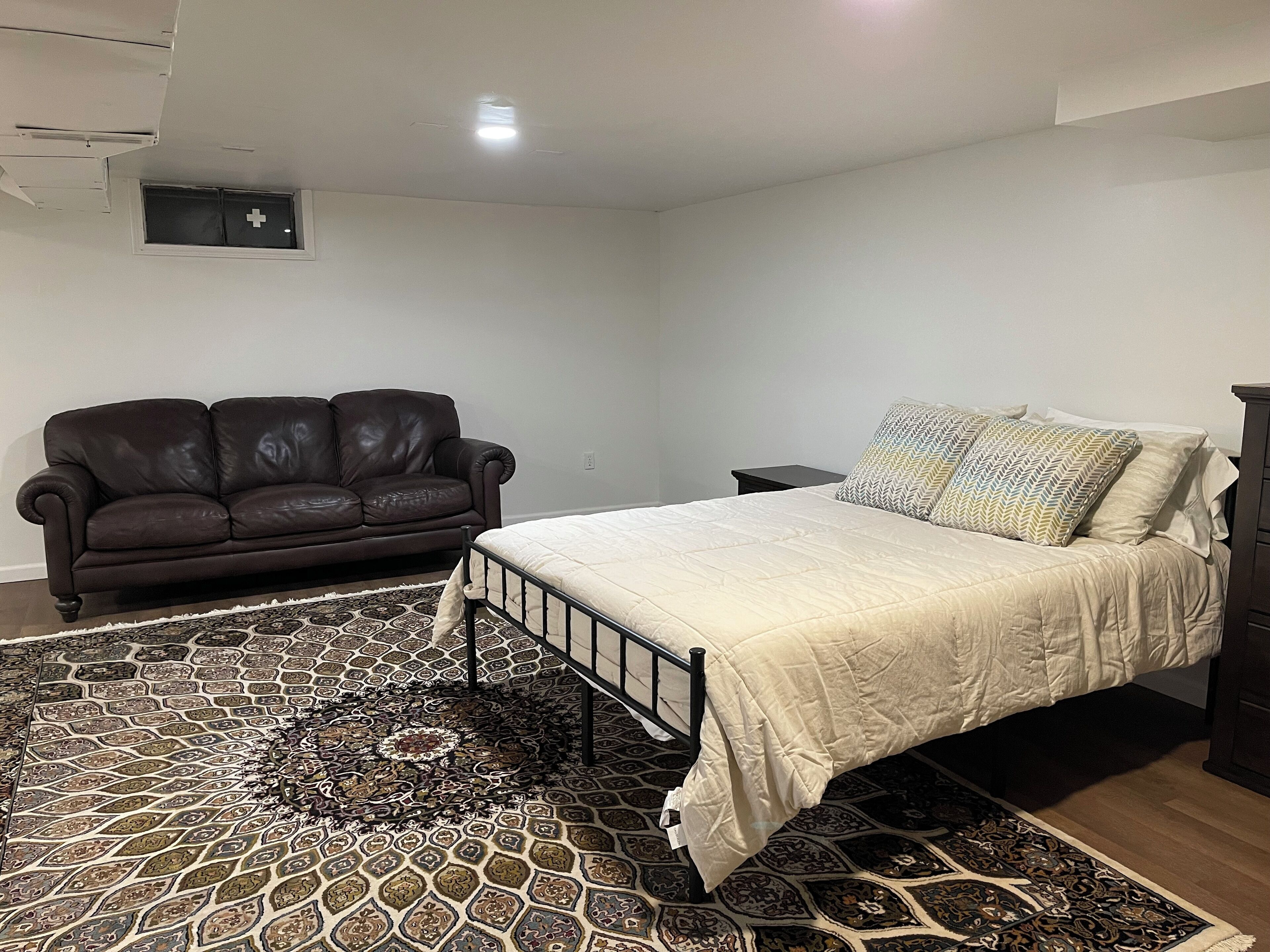 Une chambre à coucher avec un lit, un canapé en cuir marron foncé, un tapis à motifs et une petite table de chevet.