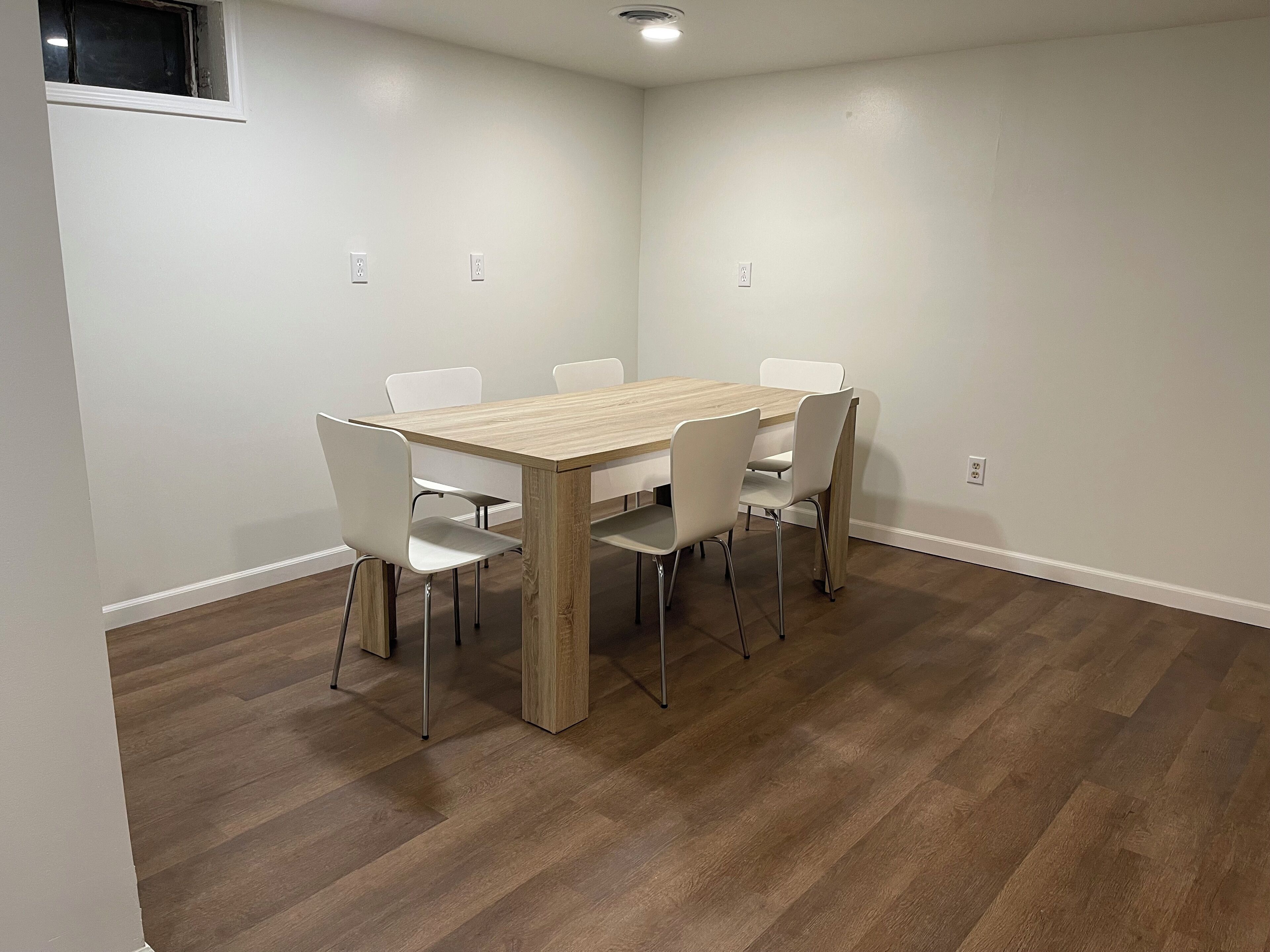 Un espace repas avec une table en bois et des chaises blanches, des murs blancs et un plancher en bois.