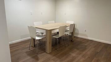 Un espace repas avec une table en bois et des chaises blanches, des murs blancs et un plancher en bois.