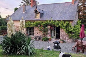 A stone house with a grey tiled roof, a small porch, and a garden with a large agave plant and a dog. - 3 Bed Cottage Sleeps 6 - Enclosed Patio -Fireplace (Beaucoudray)