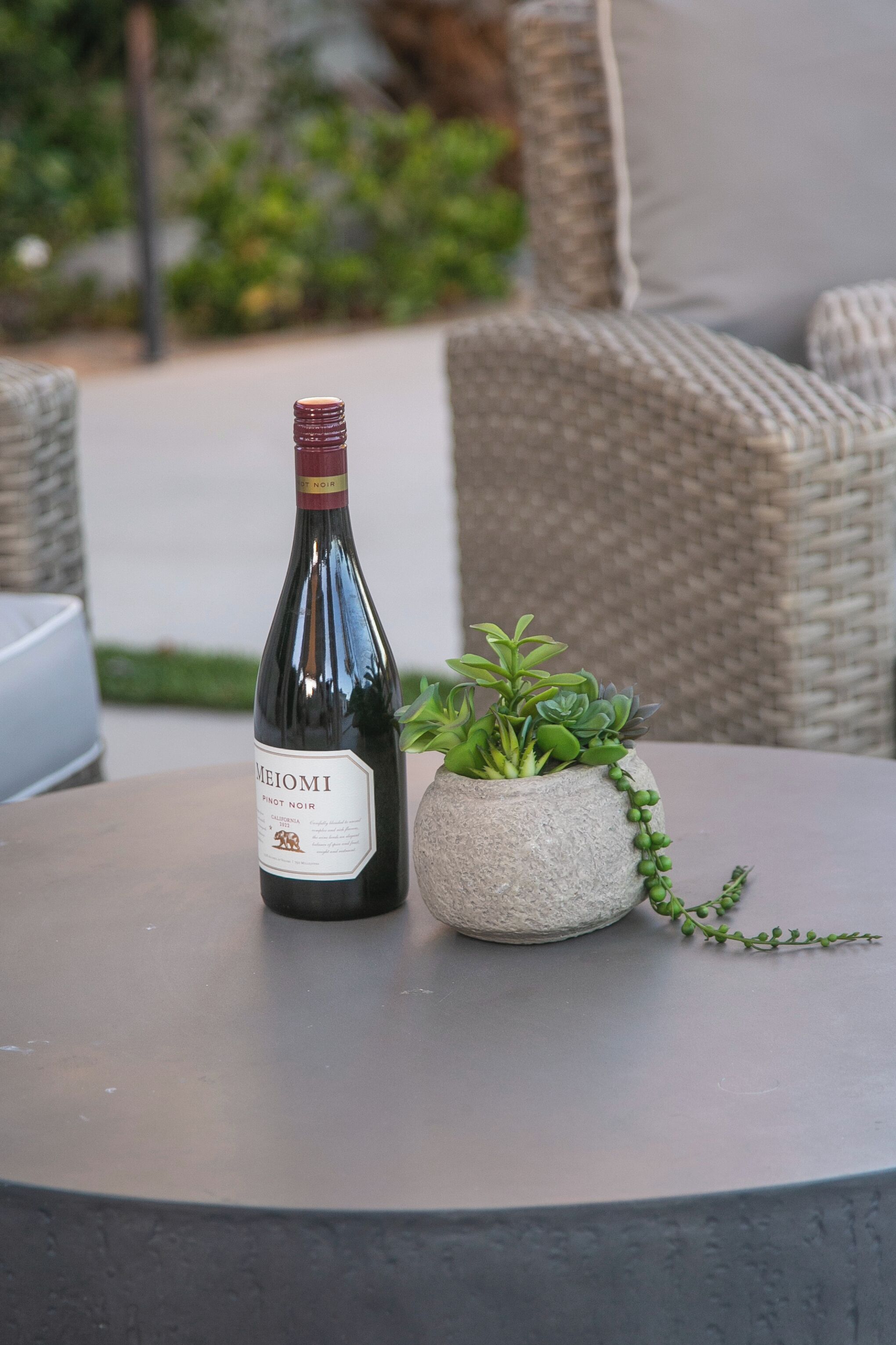 A bottle of Meimoi Pinot Noir wine on a round table with a potted plant beside it.