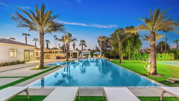 A swimming pool with lounge chairs, palm trees, and a building with large windows. - Luxury+deals,Cinema,Basketball,Volleyball, Pickleball, Putting Green,Ping Ping (Bermuda Dunes)