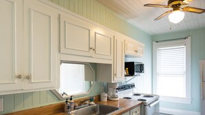A kitchen with white cabinets, a wooden countertop, a stainless steel sink, a stove, and a ceiling fan. - Pool Cottage in Historic Old Town Beaumont (Beaumont)