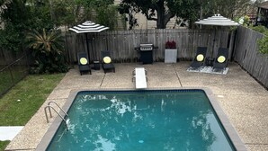 A rectangular swimming pool with a tiled edge, surrounded by a gravel area and a wooden fence. - Pool Cottage in Historic Old Town Beaumont (Beaumont)
