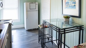 A kitchen with a refrigerator, stove, and a glass-top table with chairs. - Pool Cottage in Historic Old Town Beaumont (Beaumont)