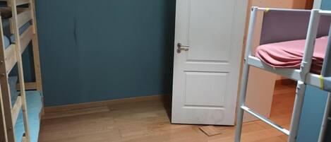A room with a wooden bunk bed, a white door, and a blue wall.