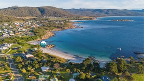 An aerial view of a coastal town with houses, a beach, and a clear view of the ocean. - Waubs Beach Cottage - Bicheno Accommodation (Glamorgan-Spring Bay)