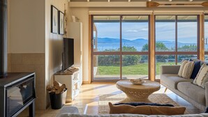 A spacious living room with a large window offering a view of the sea and mountains. - Waubs Beach Cottage - Bicheno Accommodation (Glamorgan-Spring Bay)