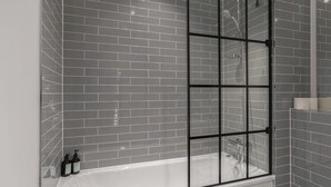 Ein modernes Badezimmer mit grauen Fliesen, einer Glasdusche und einer weißen Badewanne.