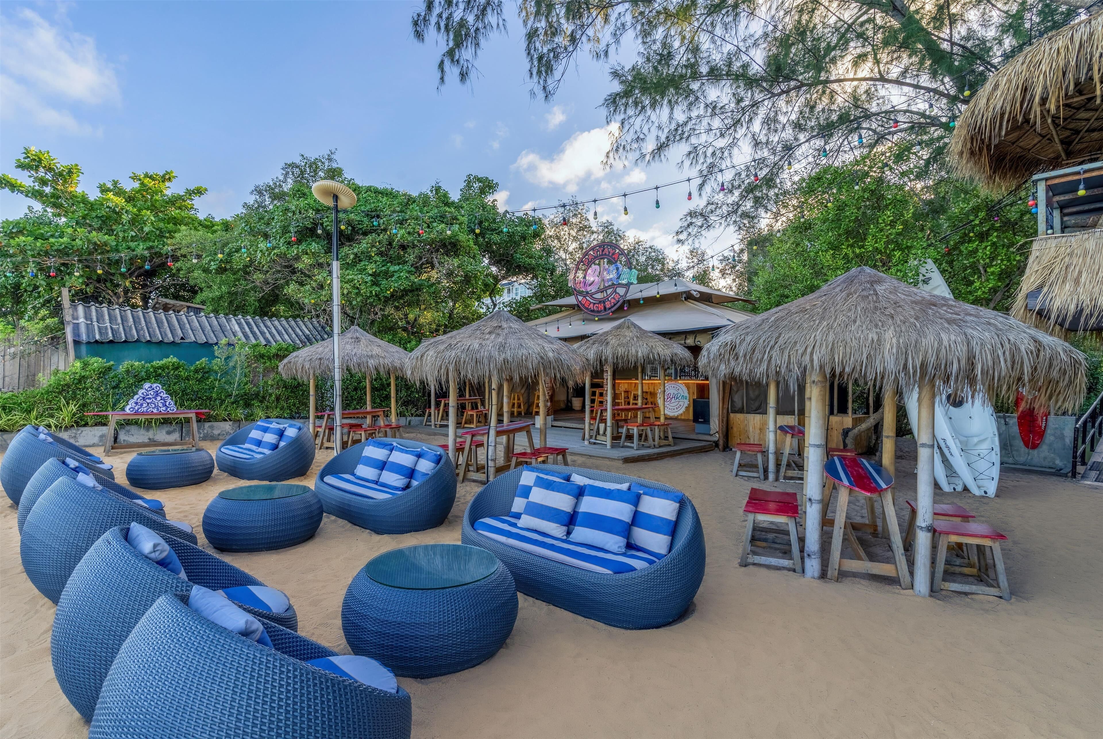 A beachside lounge area with thatched umbrellas, blue cushioned seating, and a tiki bar.