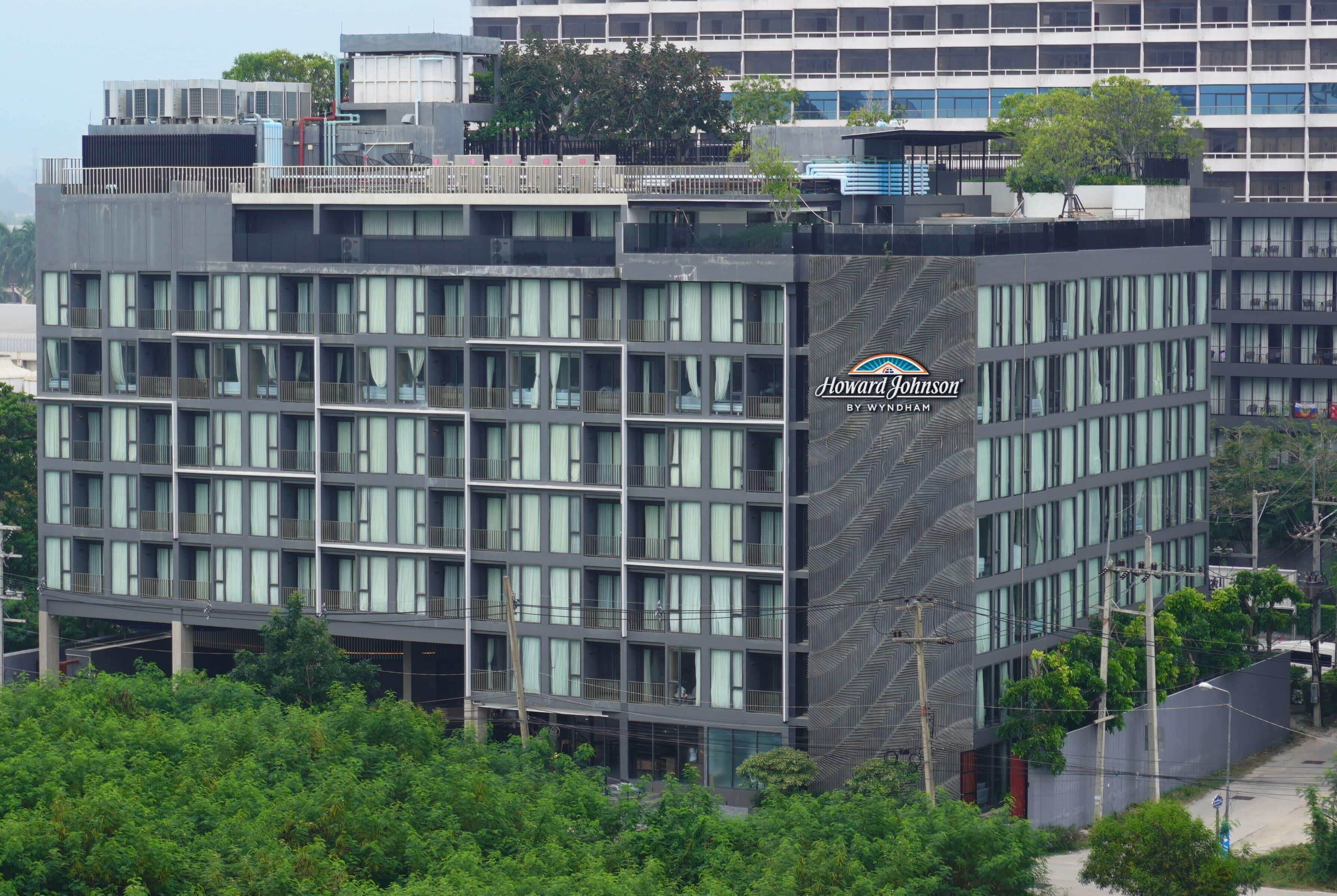 A modern hotel building with multiple floors, large windows, and a prominent logo on the side.