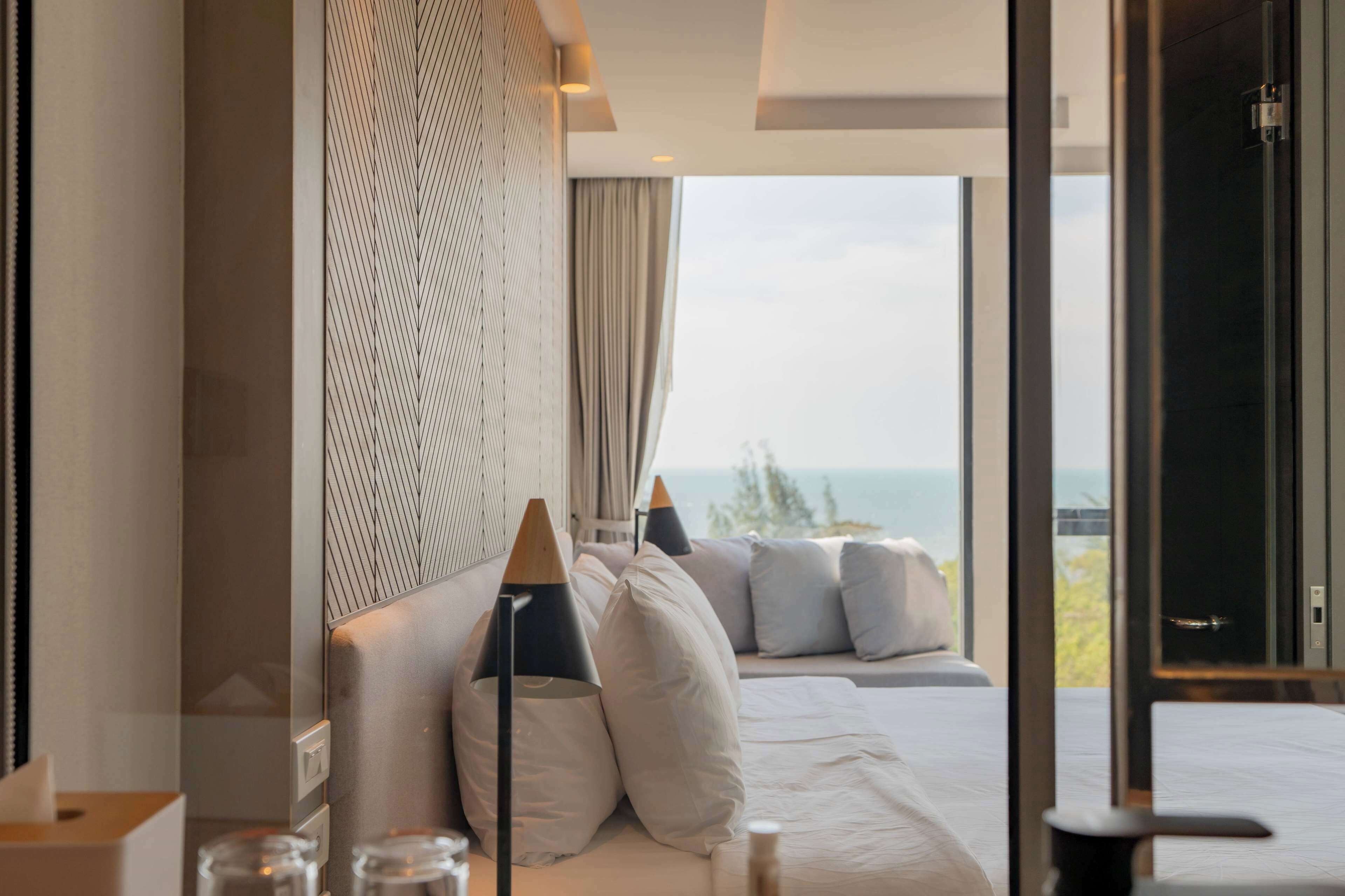A modern hotel room with a large bed, a view of the sea, and a large window.