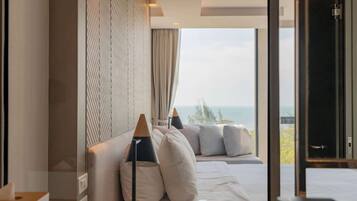A modern hotel room with a large bed, a view of the sea, and a large window.