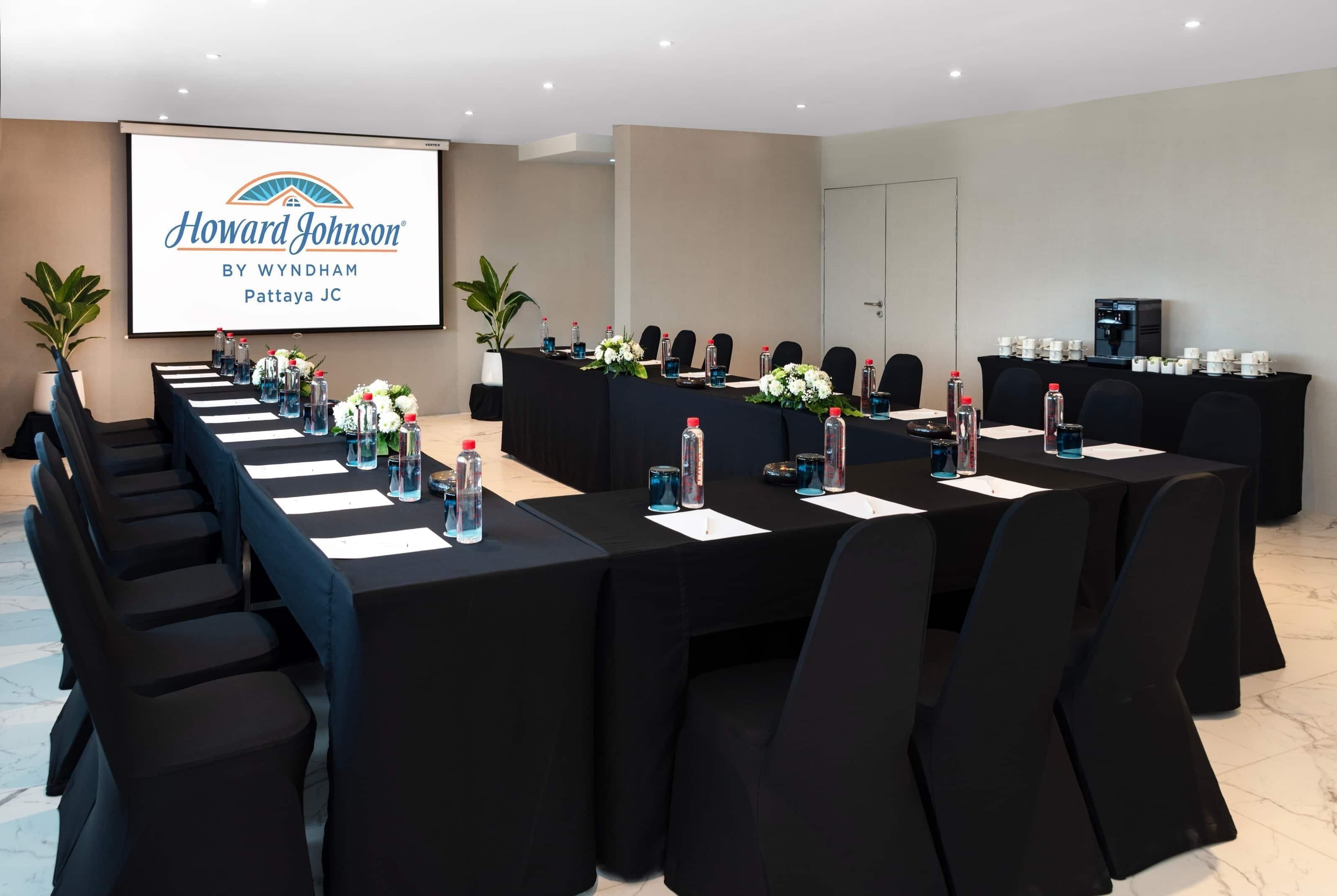A conference room with a long table, black chairs, water bottles, and a projector screen displaying a presentation.