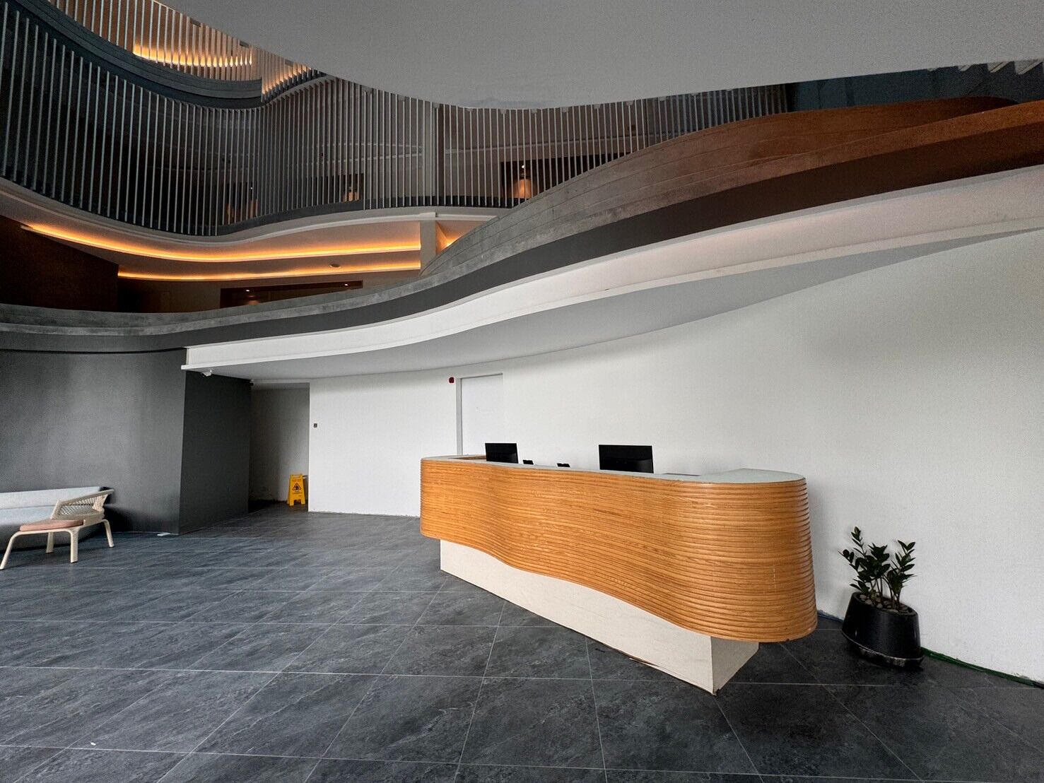 Un espace d’accueil moderne avec un comptoir en bois aux lignes courbes, un escalier et un coin salon.