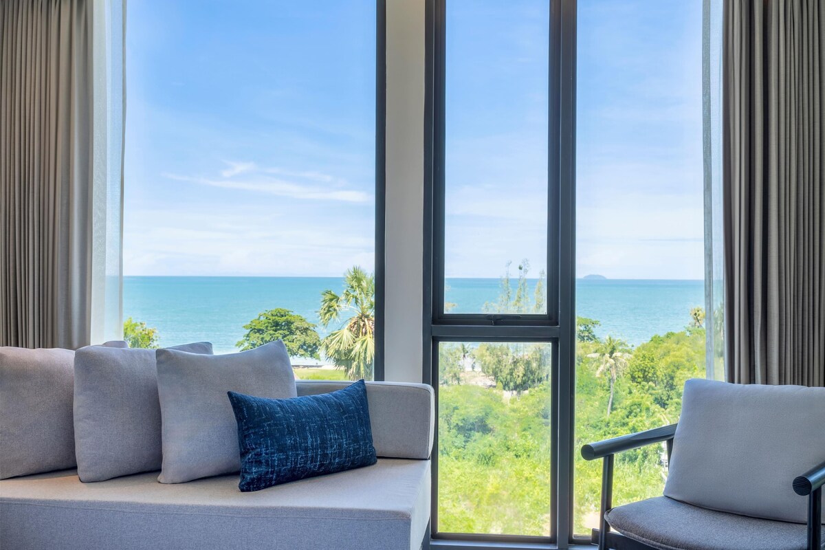 A modern living room with a large window offering a view of the ocean and greenery.