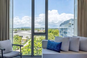 Une chambre moderne dotée d’une grande fenêtre donnant sur la ville, d’un canapé gris agrémenté d’un coussin bleu et d’un fauteuil gris.