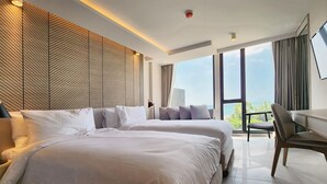 Una habitación de hotel moderna con dos camas, un ventanal grande con vistas a la ciudad, un escritorio con silla y una lámpara de pared.