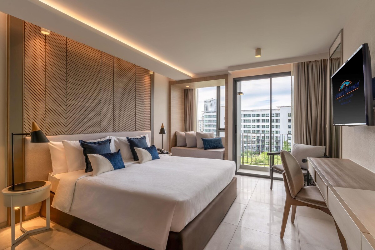 A modern hotel room with a large bed, a desk, and a TV.
