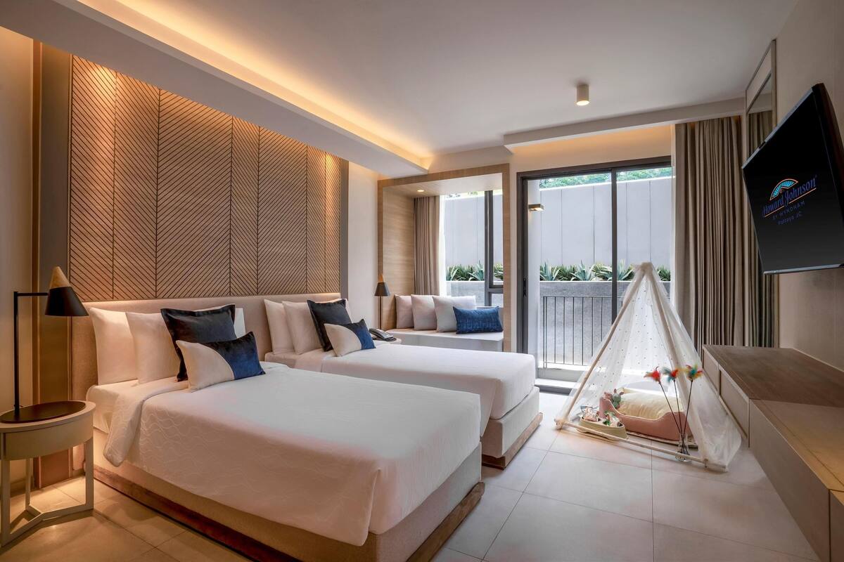 A modern hotel room with two beds, a TV, and a balcony with a view.