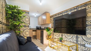 A modern living room with a sofa, a coffee table, and a TV. There is a kitchen area with cabinets and a countertop. - Luxury Versace 2 Bed, Hot Tub, Pool Table, Sky Tv (London)