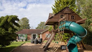 Un parque infantil con tobogán, red de escalada y casita de madera.