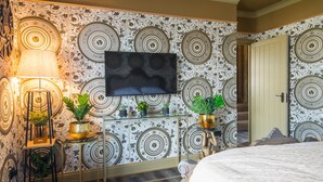 Een hotelkamer met behang met patroon, een flatscreen televisie, een bed en een klein tafeltje met planten.