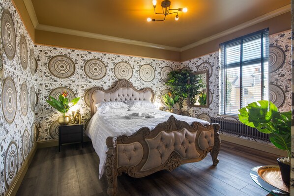 A bedroom with a large bed, a nightstand, and a potted plant.