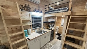 A compact kitchen with wooden walls, a built-in sink, and a window with blinds.