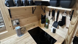 A compact kitchen with wooden walls, a black induction cooktop, and black cookware on shelves.