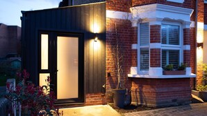 Une maison moderne avec une porte en bois foncé, une façade en briques et une baie vitrée ornée de plantes.