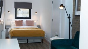Une chambre moderne avec un lit, des tables de chevet, une fenêtre donnant sur un beau paysage, une lampe sur pied et un fauteuil vert.