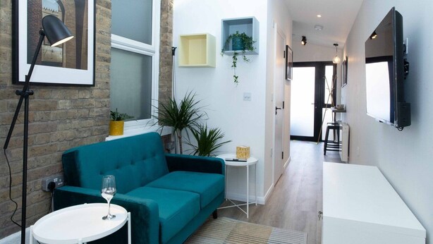 Un salon moderne avec un canapé de couleur turquoise, une petite table blanche surmontée d’un vase et un lampadaire.
