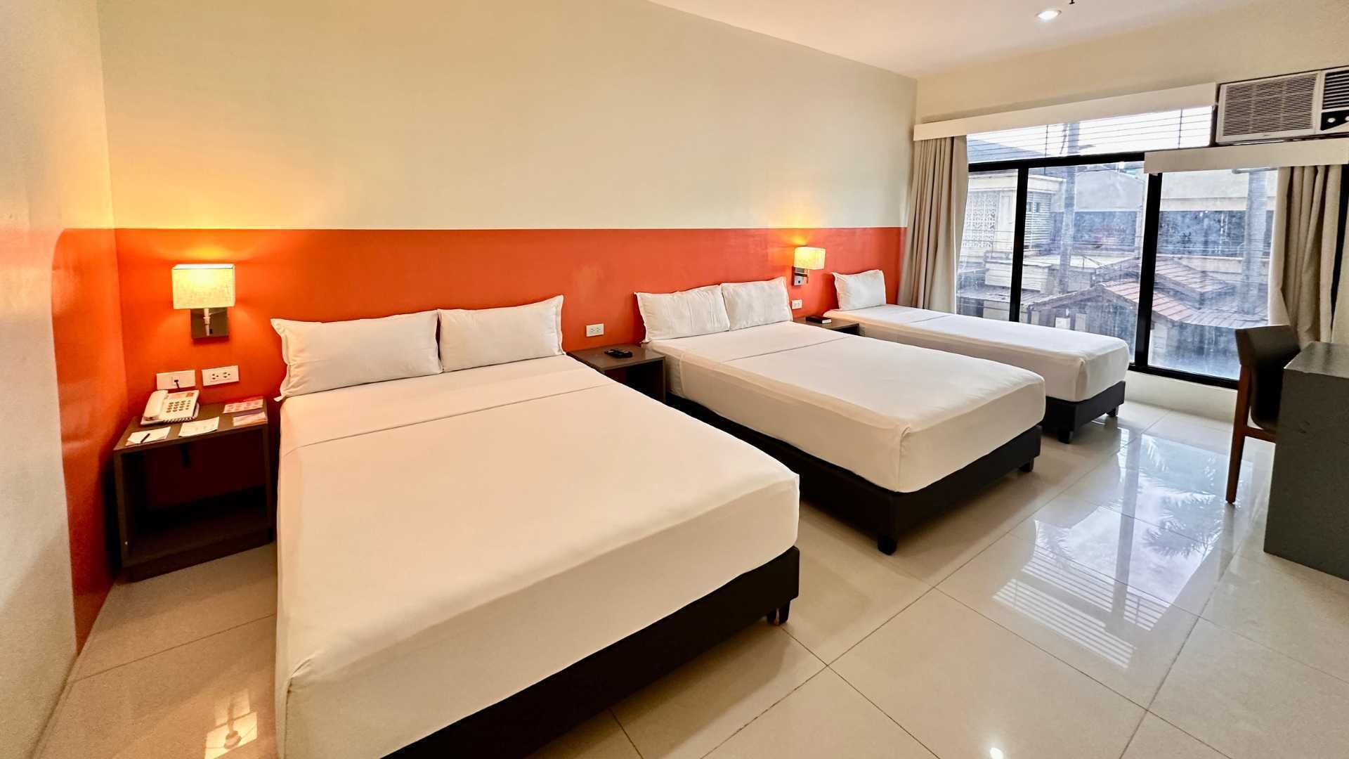 A hotel room with two beds, a desk, a phone, and a window with a view.