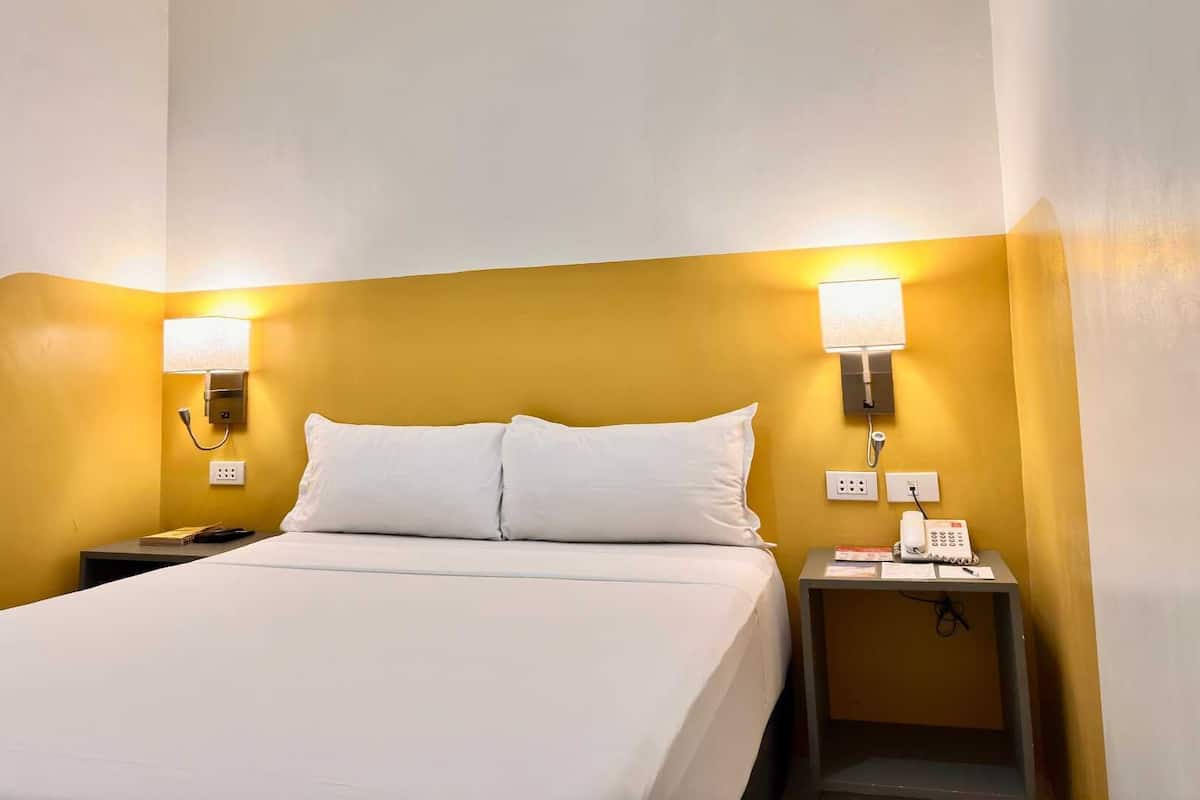 Une chambre d’hôtel avec un lit, deux lampes de chevet, un téléphone et une petite table.