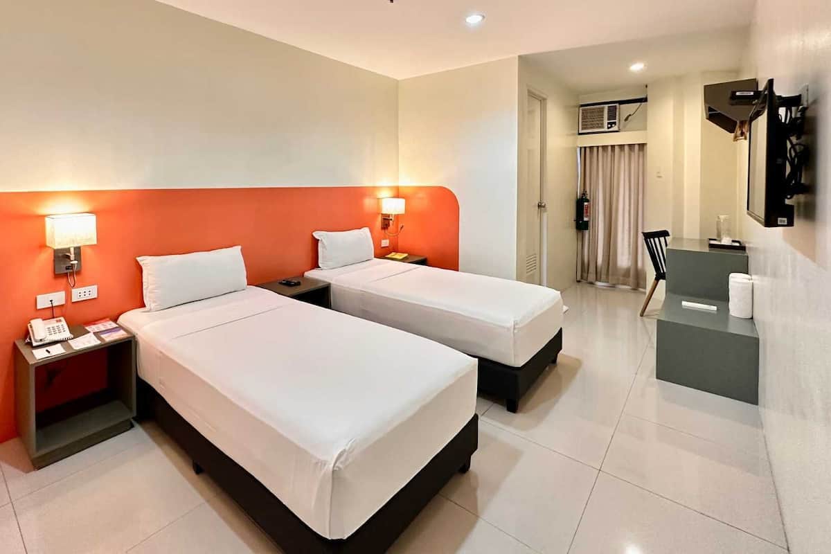 Une chambre d’hôtel avec deux lits, un bureau, une chaise et une salle de bain visible au fond.