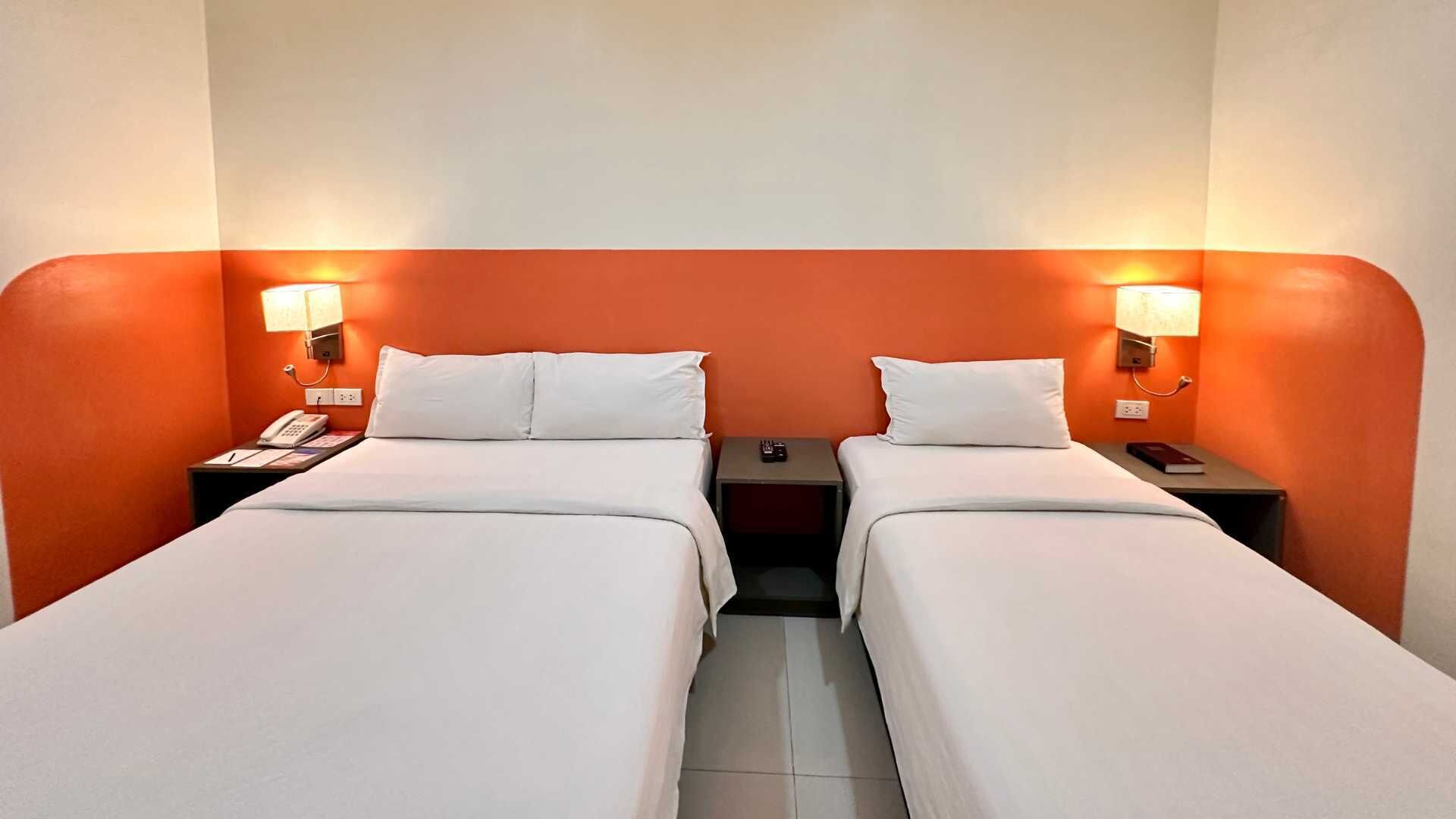 A hotel room with two single beds, each with a nightstand, a lamp, and a phone.