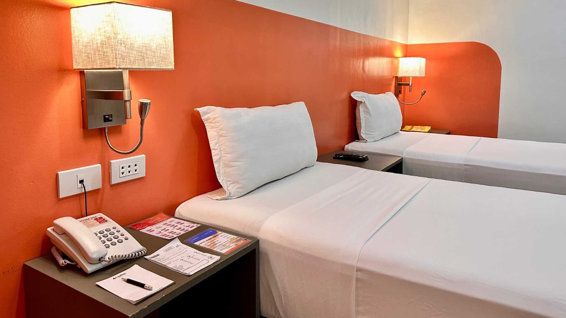 Habitación de hotel con dos camas, teléfono en la mesita de noche, lámpara y algunos papeles.