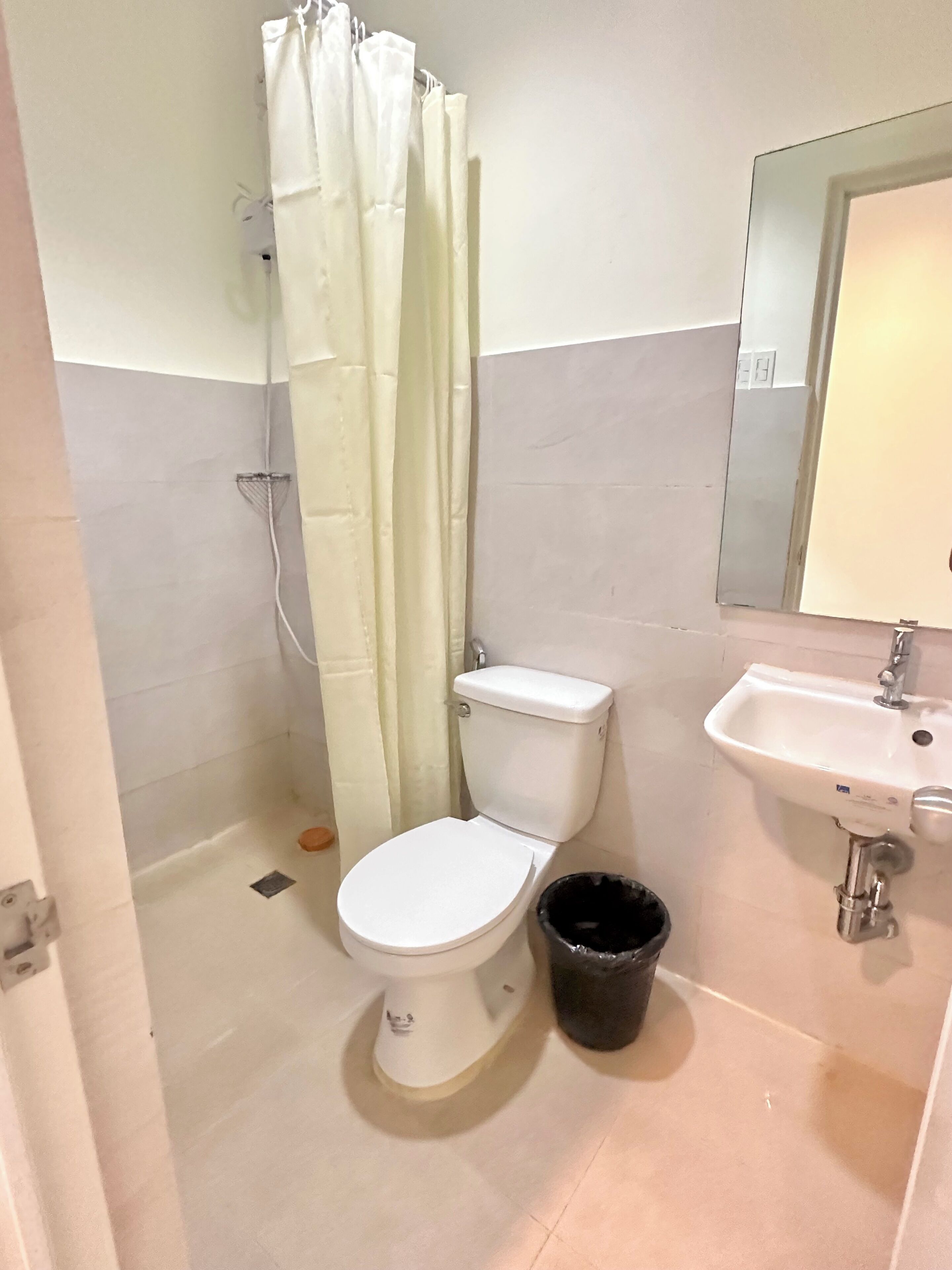 A bathroom with a toilet, a sink, a shower curtain, and a black trash bin.