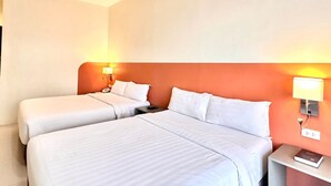 A hotel room with two beds, a nightstand with a lamp, and a wall-mounted light. - Travelbee Airport Inn (Lapu-Lapu)