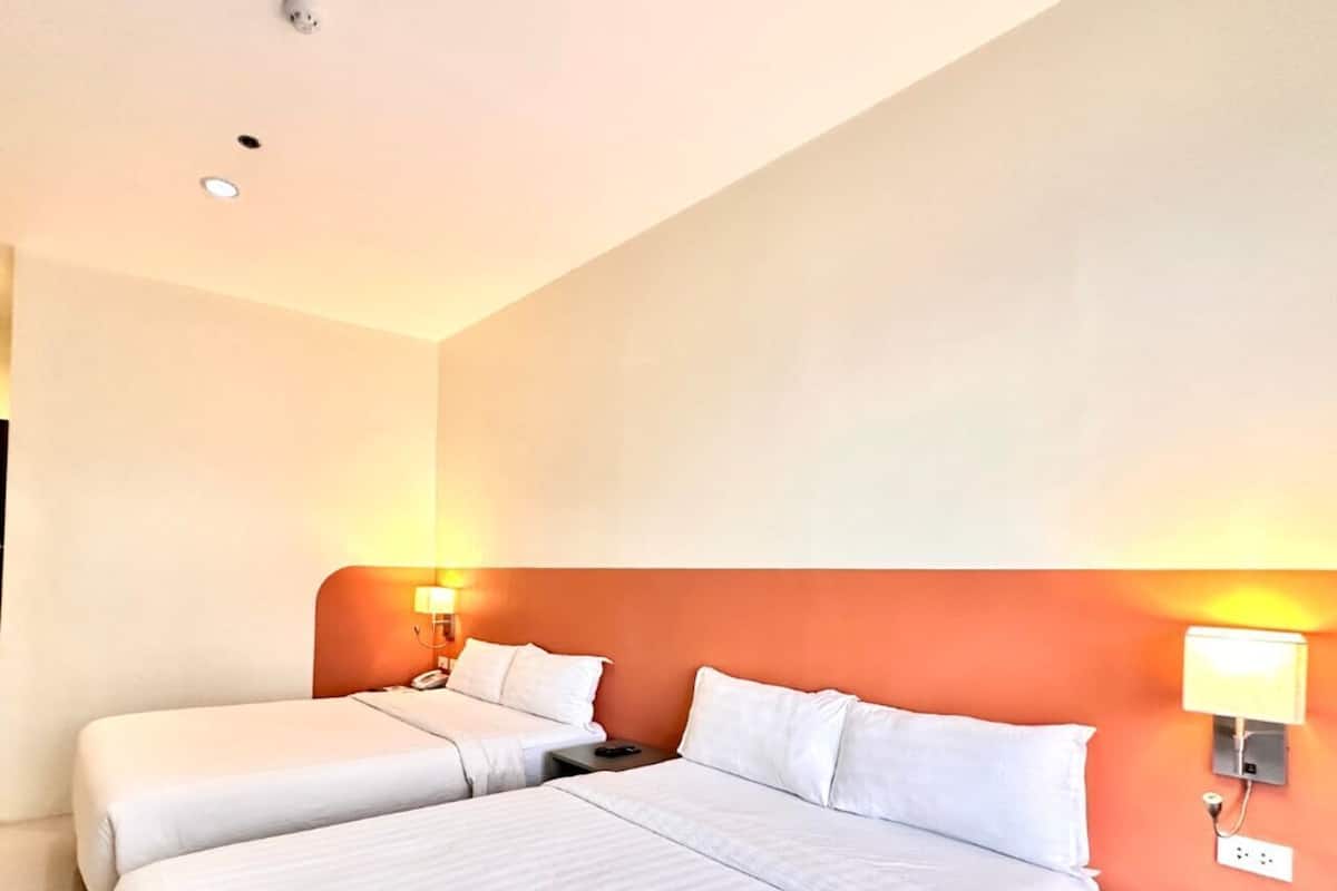 Une chambre d’hôtel avec deux lits, une table de chevet avec une lampe et un luminaire fixé au mur.