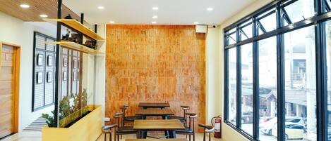 A modern restaurant interior with wooden tables and chairs, a brick accent wall, and large windows offering a city view.